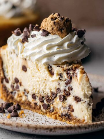 Easy Cookie Dough Cheesecake Recipe 1 Creamy cookie dough cheesecake slice topped with whipped cream, mini chocolate chips, and a mini chocolate chip cookie.