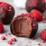 Halved Dark Chocolate Raspberry Truffles with creamy ganache center topped with freeze-dried raspberry powder and fresh raspberries.