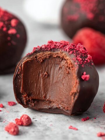Easy Dark Chocolate Raspberry Truffles 1 Halved Dark Chocolate Raspberry Truffles with creamy ganache center topped with freeze-dried raspberry powder and fresh raspberries.