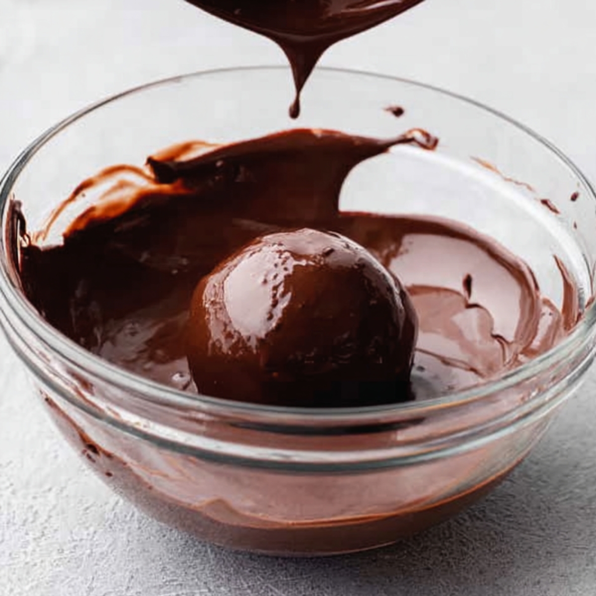 Easy Dark Chocolate Raspberry Truffles 11 Dark chocolate raspberry truffle being dipped into melted chocolate in a glass bowl before coating.