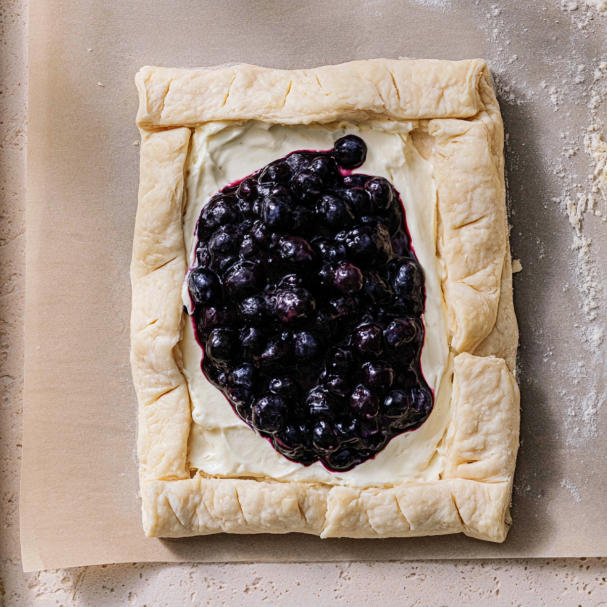 The Best Blueberry Danish Recipe 11 Unbaked blueberry Danish made with puff pastry, vanilla cream cheese filling, and homemade blueberry compote on a parchment-lined baking sheet before baking.