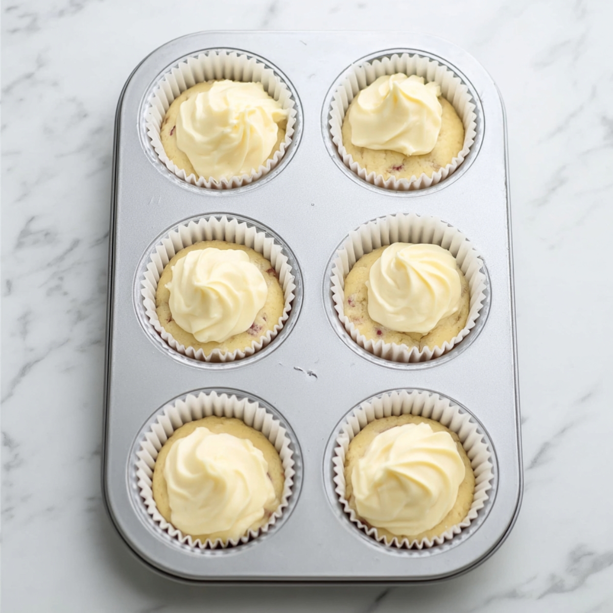 Easy Cream Cheese Banana Muffins 11 Cream cheese banana muffin batter in a lined muffin tin topped with smooth cream cheese filling before baking.