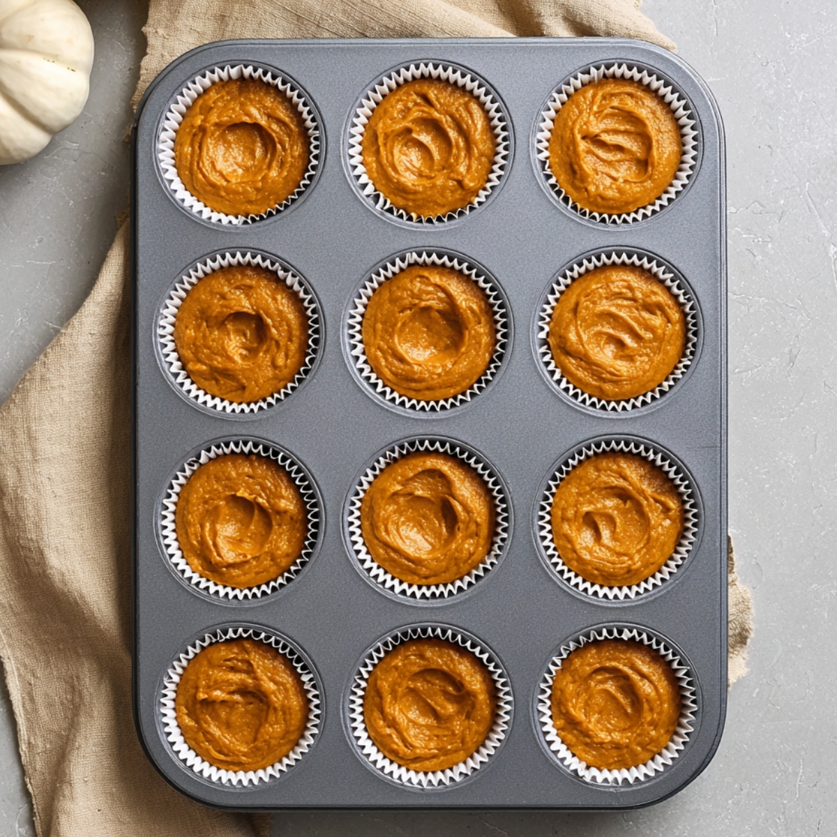 Easy Pumpkin Cream Cheese Muffins Recipe 11 Pumpkin muffin batter evenly divided into white paper liners in a 12-cup muffin pan before baking.