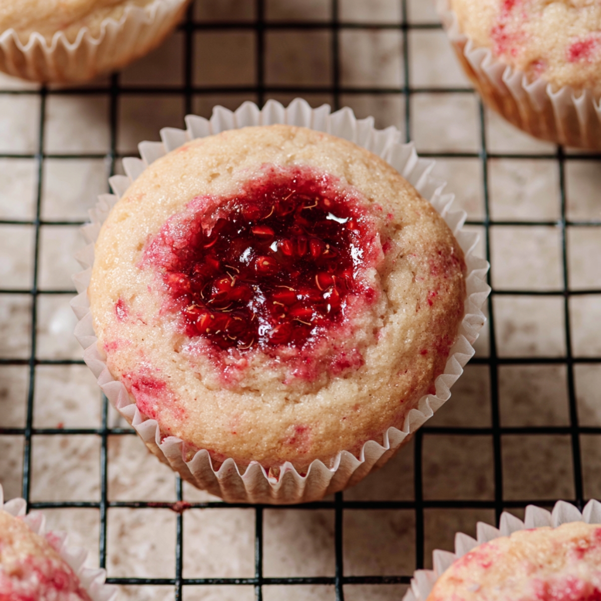 Best Raspberry Filled Cupcakes Recipe 11 Freshly baked raspberry cupcake with a glossy homemade raspberry jam filling in the center, cooling on a wire rack in a white paper liner.