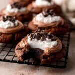 Homemade French Silk Pie Cookies topped with chocolate mousse, whipped cream, and chocolate curls on a cooling rack, with one cookie showing a fudgy bite.