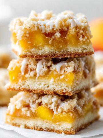 Fresh Peach Crumb Bars Recipe 2 Stack of homemade Fresh Peach Crumb Bars with buttery shortbread crust, juicy peach filling, crumb topping, and vanilla glaze.