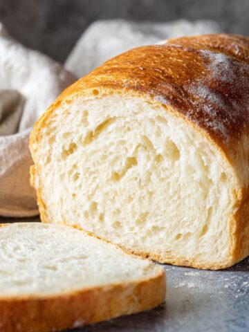 Homemade Italian Bread Recipe 1 Freshly baked homemade Italian Bread loaf with a golden crust and soft fluffy crumb, served with a sliced piece.