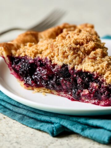 Easy Huckleberry Pie Recipe 1 Slice of huckleberry pie with a buttery crumb topping and juicy berry filling served on a white plate with a teal napkin.