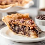 Slice of homemade Kentucky Derby Pie with gooey chocolate filling, toasted pecans, and a flaky buttery crust on a white plate.