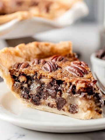 Easy Kentucky Derby Pie Recipe 2 Slice of homemade Kentucky Derby Pie with gooey chocolate filling, toasted pecans, and a flaky buttery crust on a white plate.