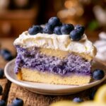 Slice of Lemon Blueberry Mousse Cake with fluffy whipped cream frosting and fresh blueberries, showcasing vibrant blueberry layers on a rustic wooden table.
