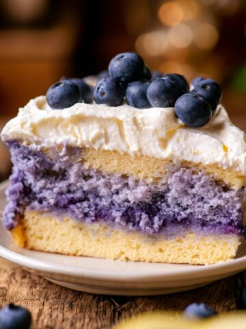Lemon Blueberry Mousse Cake 3 Slice of Lemon Blueberry Mousse Cake with fluffy whipped cream frosting and fresh blueberries, showcasing vibrant blueberry layers on a rustic wooden table.