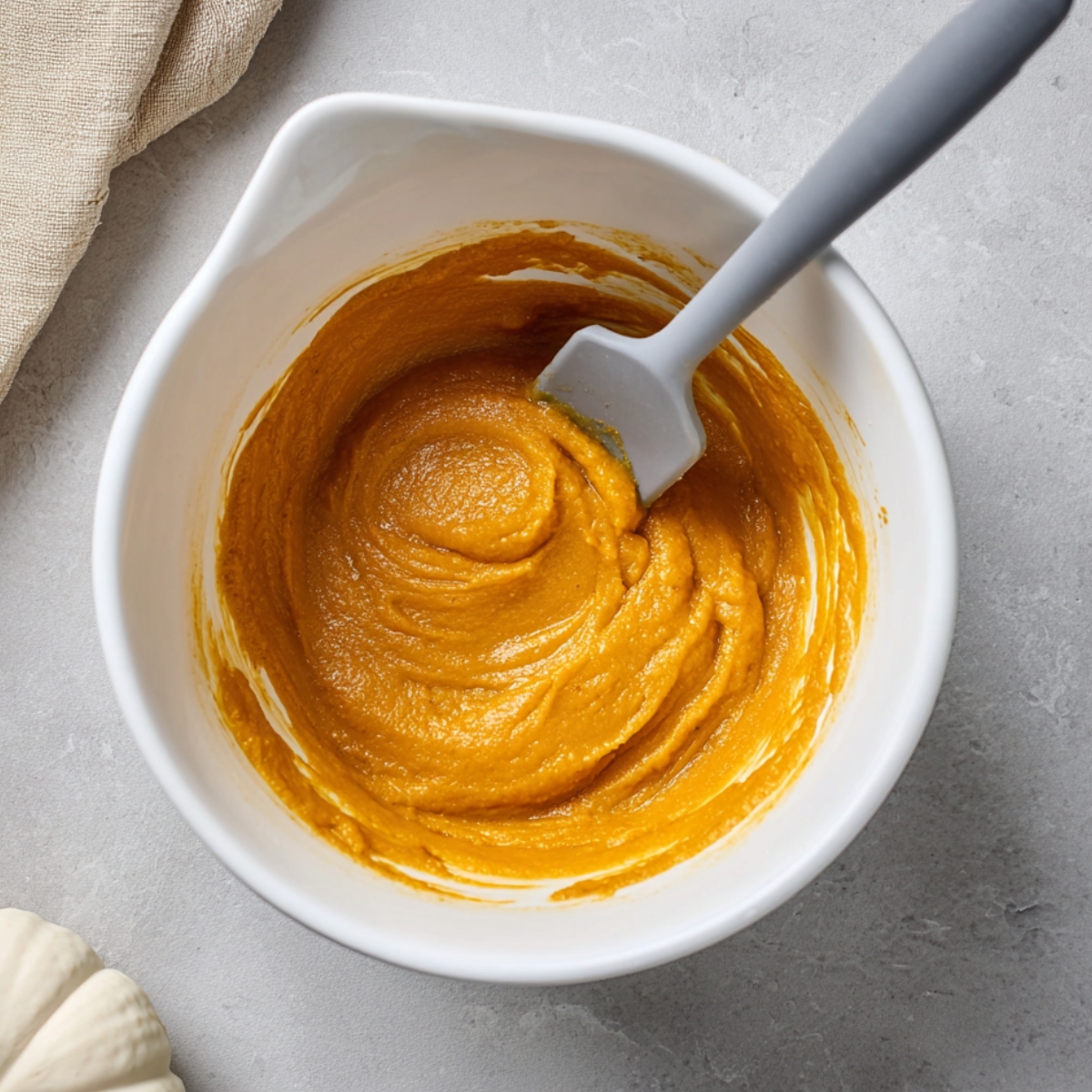 Easy Pumpkin Cream Cheese Muffins Recipe 10 Smooth homemade pumpkin muffin batter mixed in a white bowl with a silicone spatula, ready for baking.