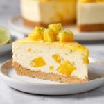 Slice of Mango Mousse Cake with coconut sablé crust, creamy mango mousse, fresh mango chunks, and lime zest garnish on a dessert plate.