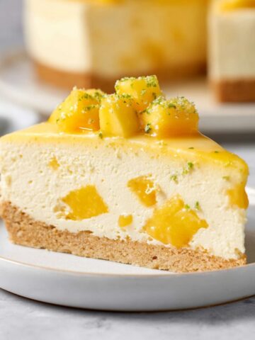 Easy Mango Mousse Cake Recipe 1 Slice of Mango Mousse Cake with coconut sablé crust, creamy mango mousse, fresh mango chunks, and lime zest garnish on a dessert plate.