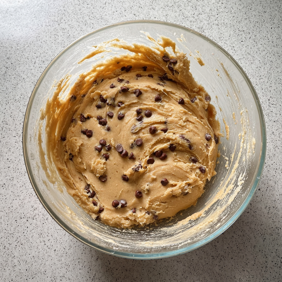 Easy Cookie Dough Cheesecake Recipe 10 Homemade edible chocolate chip cookie dough mixed in a glass bowl, ready to layer into a cookie dough cheesecake.