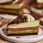 Slice of No Bake Dubai Chocolate Cheesecake with chocolate cookie crust, crispy pistachio knafeh, chocolate ganache, and creamy pistachio cheesecake filling.