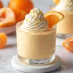 Creamy Orange Mousse Cups served in a glass dessert cup topped with whipped cream, orange slice, and fresh orange zest.