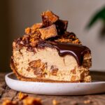 Slice of no-bake peanut butter Butterfinger pie with chocolate ganache, graham cracker crust, and crushed Butterfinger candy on a white plate.