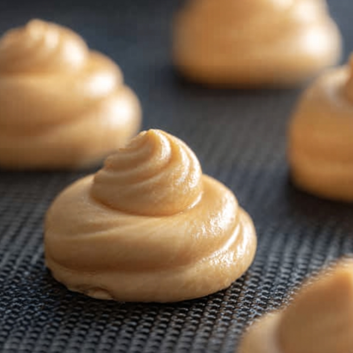 French Choux au Craquelin 11 Smooth piped choux pastry rounds on a silicone baking mat ready for baking into cream puffs.
