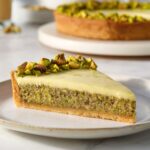 Slice of triple Pistachio Tart with buttery crust, moist pistachio sponge, silky pistachio cream, and chopped pistachio topping.