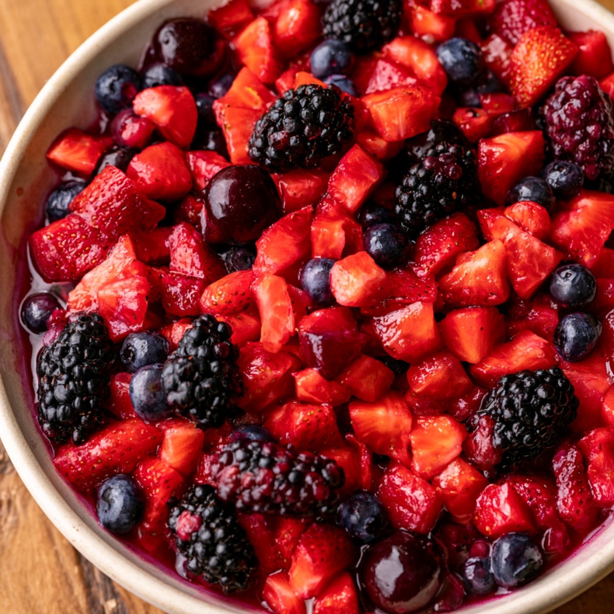 Easy Berries and Cream Cake Recipe 11 Fresh mixed berries including strawberries, blueberries, blackberries, and cherries chopped and combined in a bowl for a homemade berries and cream cake filling.