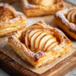 Golden Puff Pastry Apple Tartlets filled with cinnamon applesauce, topped with thinly sliced baked apples, and dusted with powdered sugar.