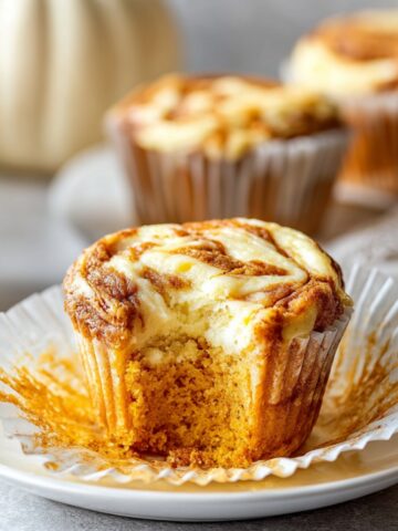 Easy Pumpkin Cream Cheese Muffins Recipe 1 Pumpkin Cream Cheese Muffins with a bite taken out, showing its moist pumpkin crumb and creamy cheesecake swirl topping.