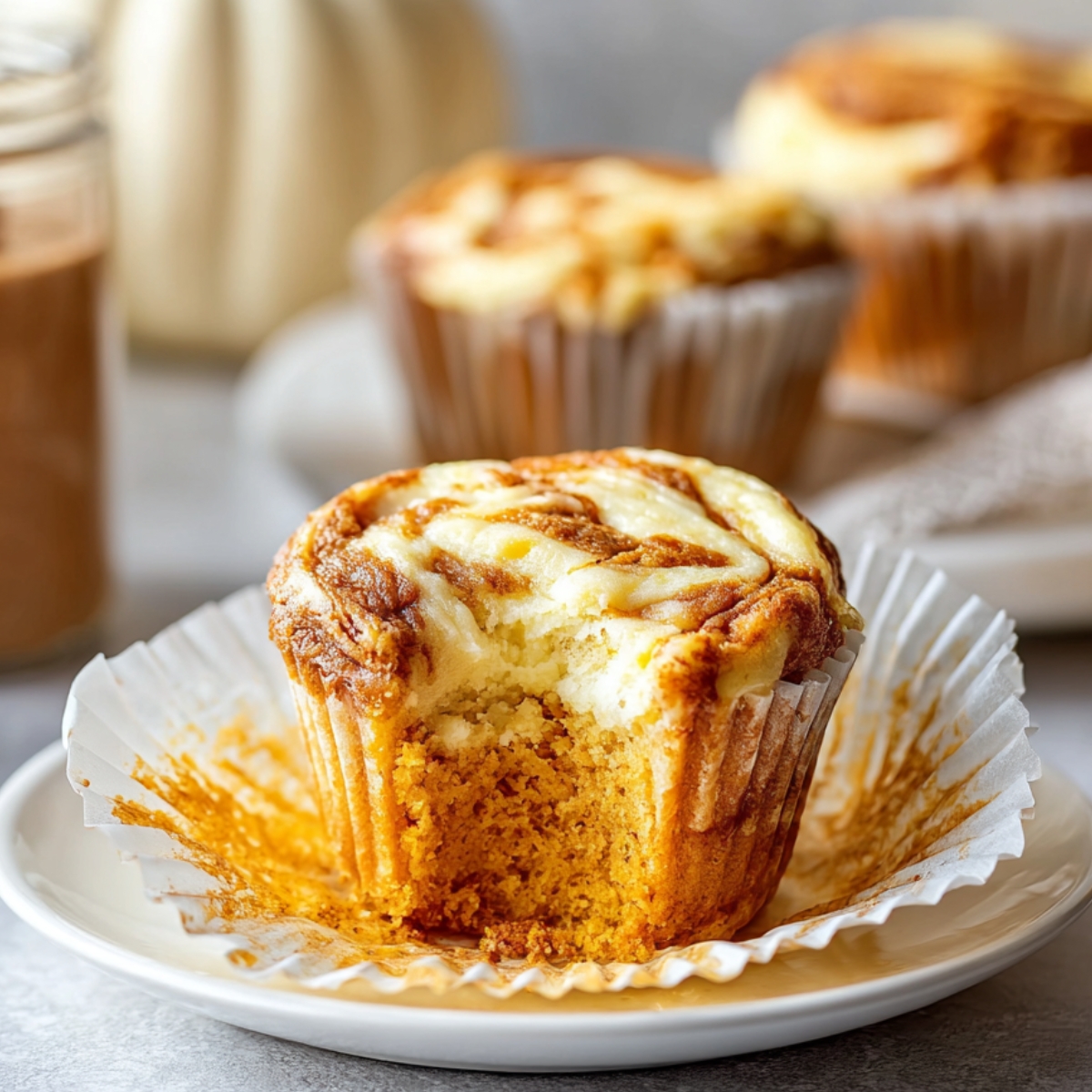 Easy Pumpkin Cream Cheese Muffins Recipe 9 Pumpkin Cream Cheese Muffins with a bite taken out, showing its moist pumpkin crumb and creamy cheesecake swirl topping.