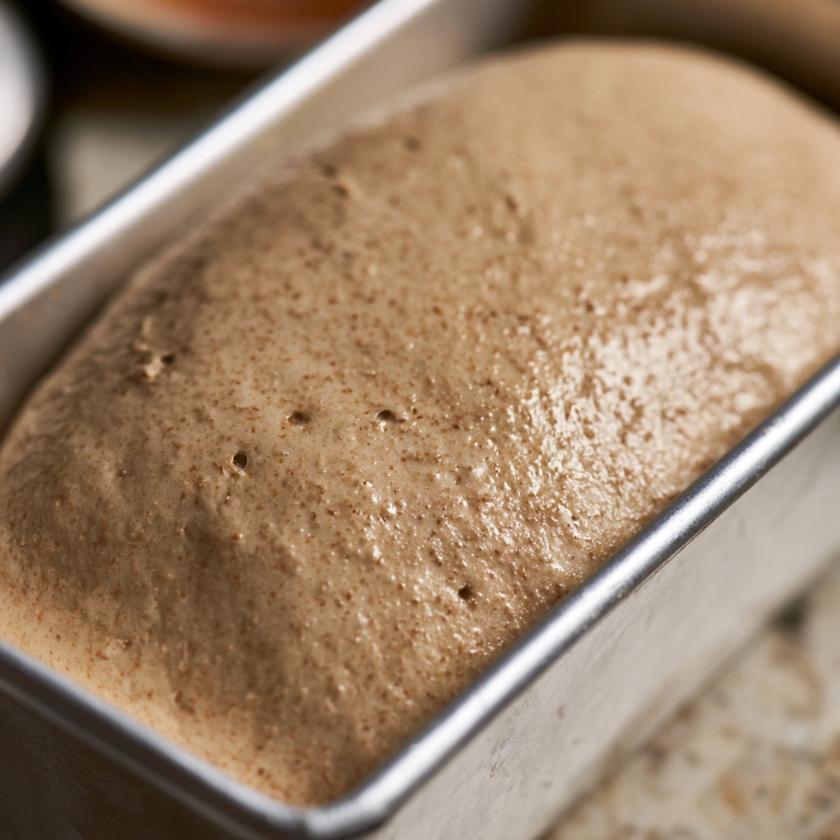 Homemade Ezekiel Bread Recipe 11 Ezekiel bread dough after the second rise in a loaf pan, fully proofed with a smooth domed top and tiny air bubbles, ready for baking.