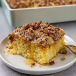 Moist Texas Tornado Cake topped with warm coconut pecan frosting served on a white dessert plate.