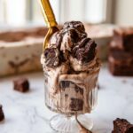 Homemade Brownie Batter Ice Cream served in a vintage glass dessert cup with fudgy brownie pieces, chocolate sauce, and a gold spoon.
