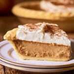 Slice of creamy cinnamon pie topped with whipped cream and a dusting of ground cinnamon on a dessert plate.