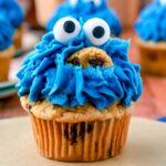 Homemade Cookie Monster Cupcakes with bright blue frosting, candy eyes, and chocolate chip cookies on top.