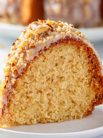 Easy Louisiana Crunch Cake Recipe 1 Slice of Louisiana Crunch Cake topped with vanilla glaze and chopped almonds on a white plate.