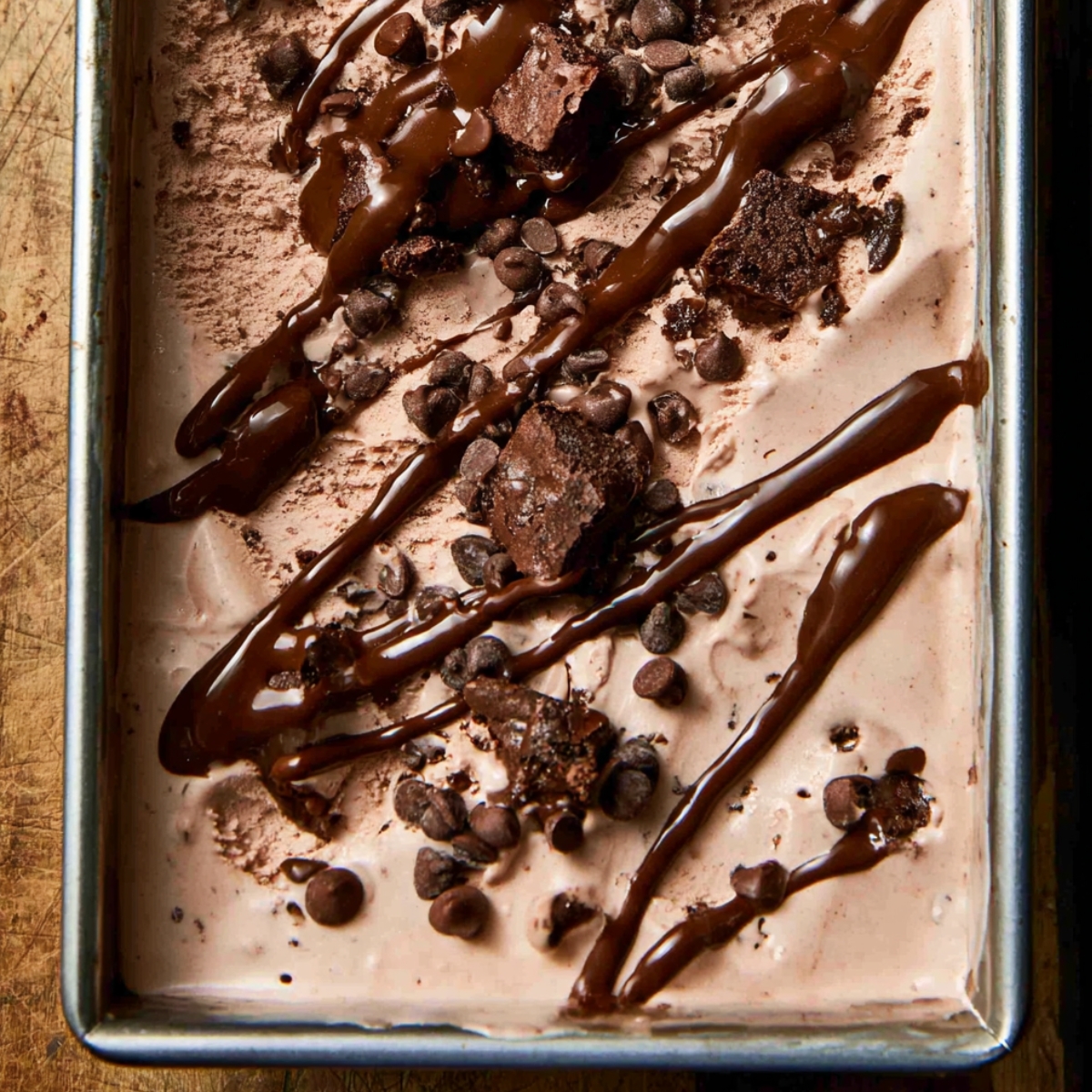Easy Brownie Batter Ice Cream Recipe 11 Brownie batter ice cream in a loaf pan topped with fudgy brownie chunks, mini chocolate chips, and rich chocolate drizzle before freezing.