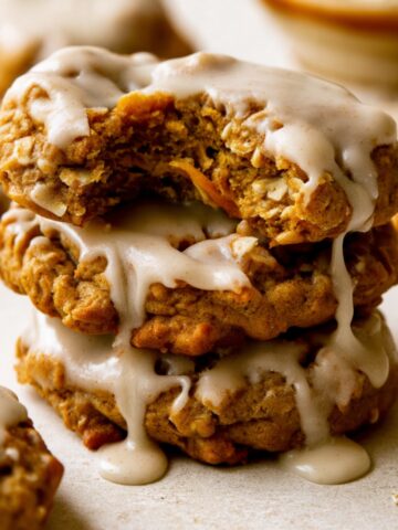 Brown Butter Pumpkin Oatmeal Cookies 3 Stack of homemade Brown Butter Pumpkin Oatmeal Cookies topped with rich brown butter glaze, featuring a broken cookie that reveals a soft, chewy oatmeal and pumpkin filling.