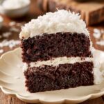 Slice of moist Chocolate Coconut Cake with cream cheese frosting and shredded coconut on a dessert plate.