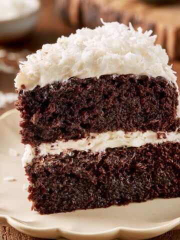 Easy Chocolate Coconut Cake Recipe 2 Slice of moist Chocolate Coconut Cake with cream cheese frosting and shredded coconut on a dessert plate.