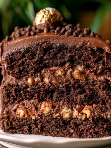 Easy Ferrero Rocher Cake Recipe 1 Thick slice of Ferrero Rocher Cake with moist chocolate layers, creamy chocolate frosting, crunchy hazelnut filling, and Ferrero Rocher candy on top.