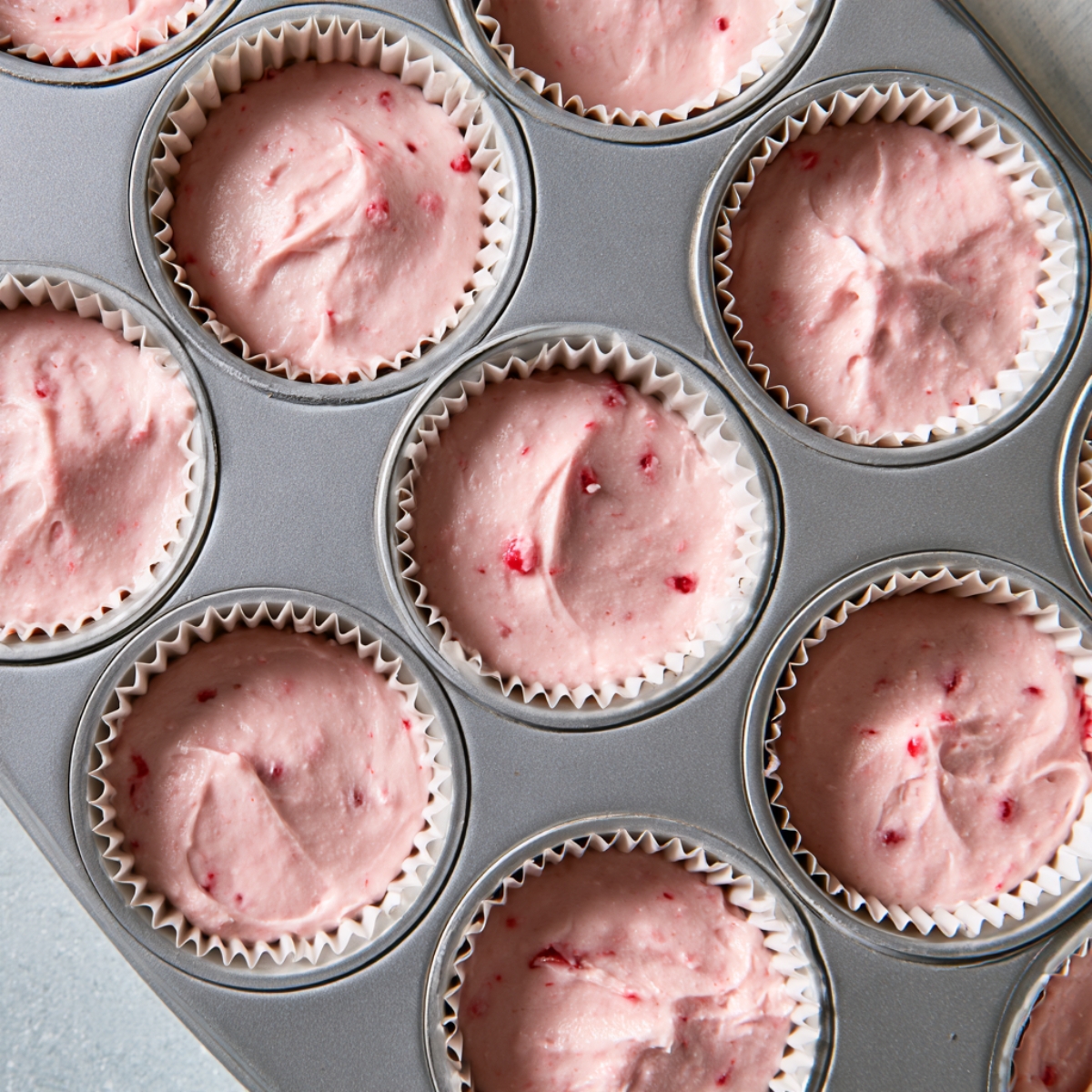 Soft Maraschino Cherry Cupcakes Recipe 11 Pink cherry cupcake batter portioned into white cupcake liners in a metal muffin tin.