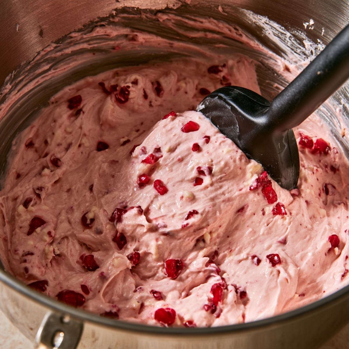 Soft Maraschino Cherry Cupcakes Recipe 10 Pink cupcake batter with chopped maraschino cherries being folded into the mixture with a spatula.