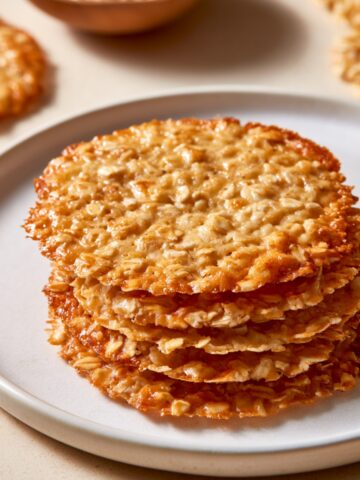 Easy Oatmeal Lace Cookies Recipe 1 Stack of thin, crisp golden Oatmeal Lace Cookies on a white plate.