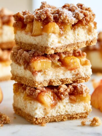 Easy Peach Cobbler Cheesecake Bars Recipe 2 Peach cobbler cheesecake bars stacked with a buttery graham cracker crust, creamy cheesecake filling, juicy peaches, and cinnamon streusel topping.
